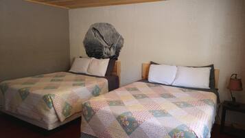 Une chambre avec deux lits, chacun recouvert d’une courtepointe matelassée et agrémenté d’oreillers. Le lit situé à gauche est doté d’une tête de lit en bois, et le lit à droite est accompagné d’une table de chevet avec une lampe.