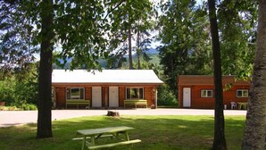 Una cabaña rústica de madera con un porche y una mesa de picnic en un área boscosa.