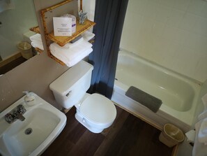 A bathroom with a toilet, sink, and bathtub. There is a shelf with towels and a sign. - Overlook Inn & Cabins (Clearwater)