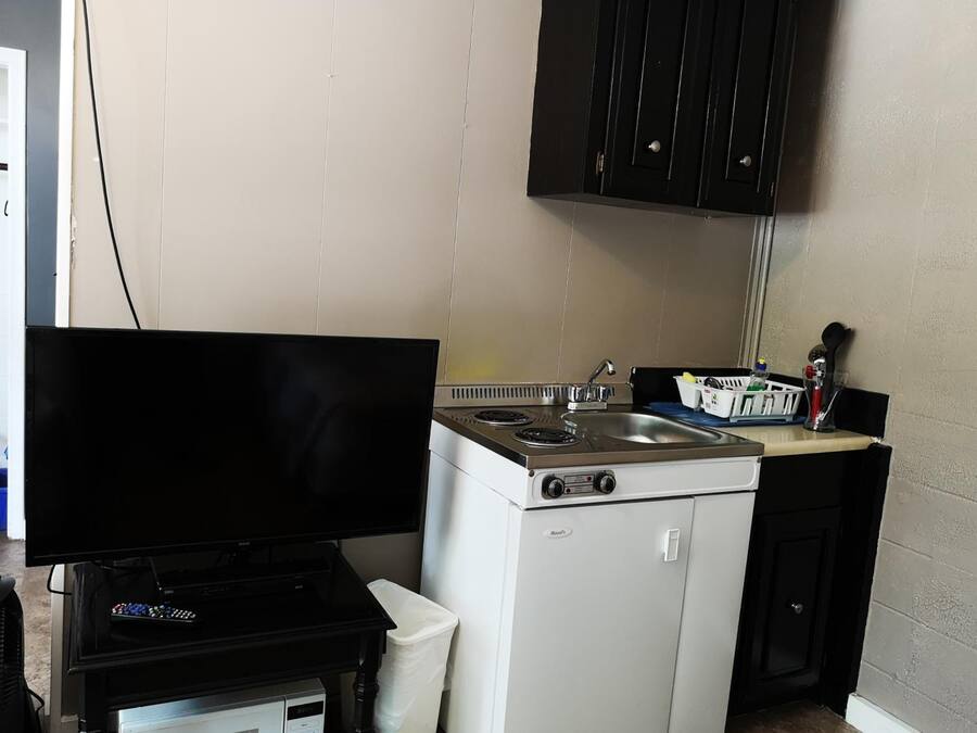A compact kitchen with a stove, sink, and a television on a stand.