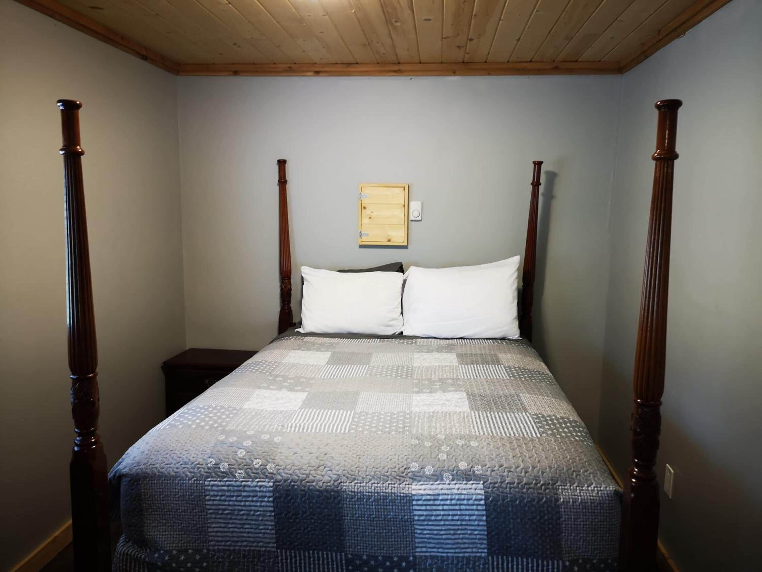 A four-poster bed with a quilted bedspread, a wooden headboard, and a small bedside table.