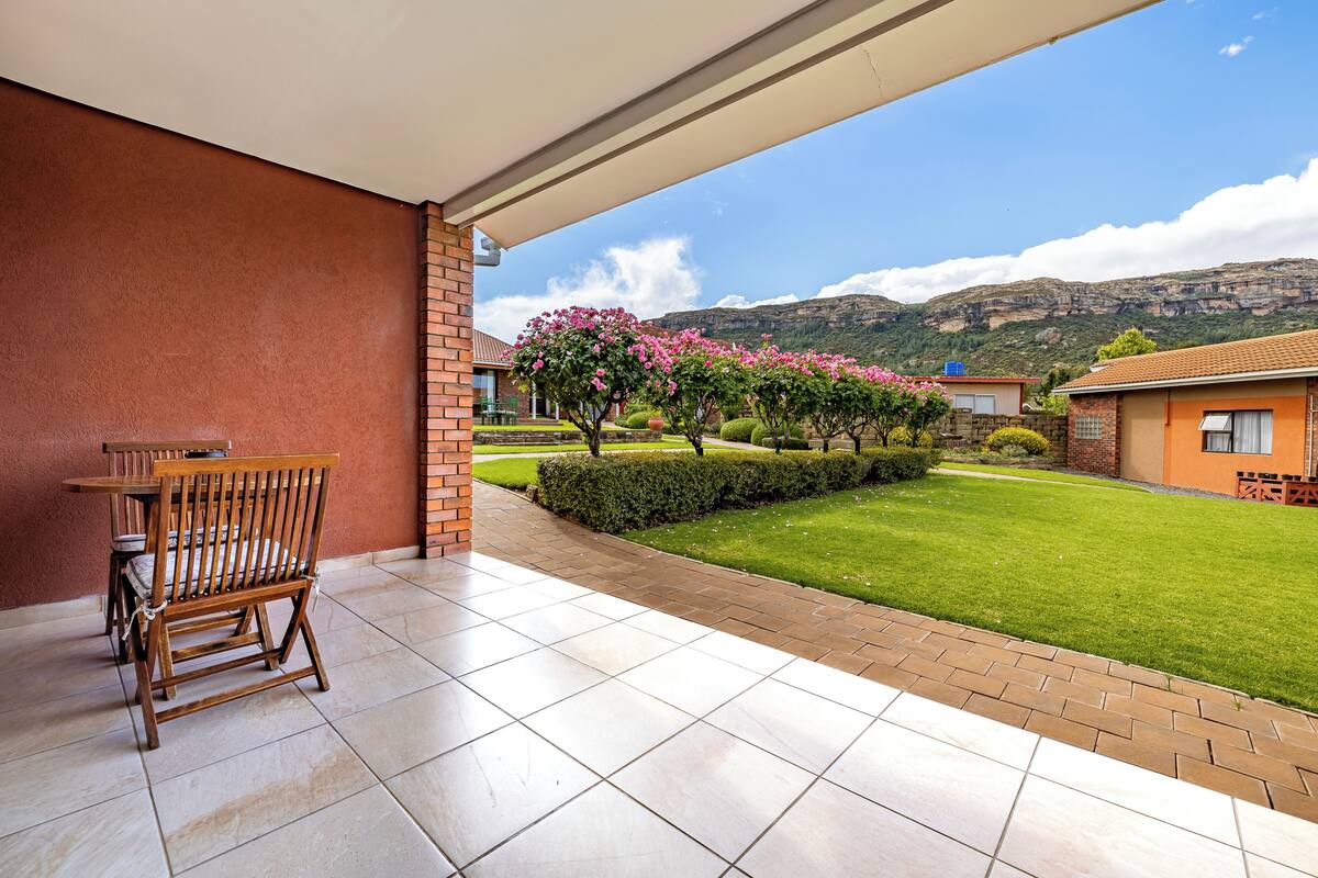 A covered patio with a table and chairs, a well-maintained lawn, and a view of a mountain range.