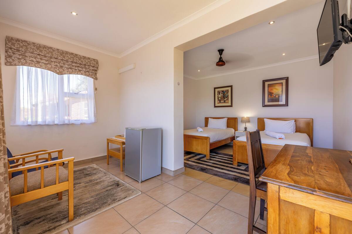 A hotel room with a bed, a desk, a chair, a refrigerator, and a television.