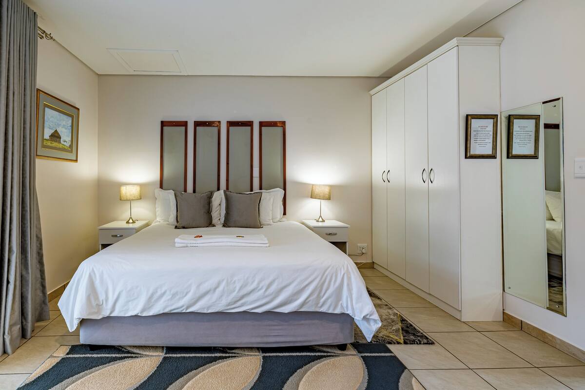 A hotel room with a bed, bedside lamps, a nightstand, a wardrobe, and a large mirror.