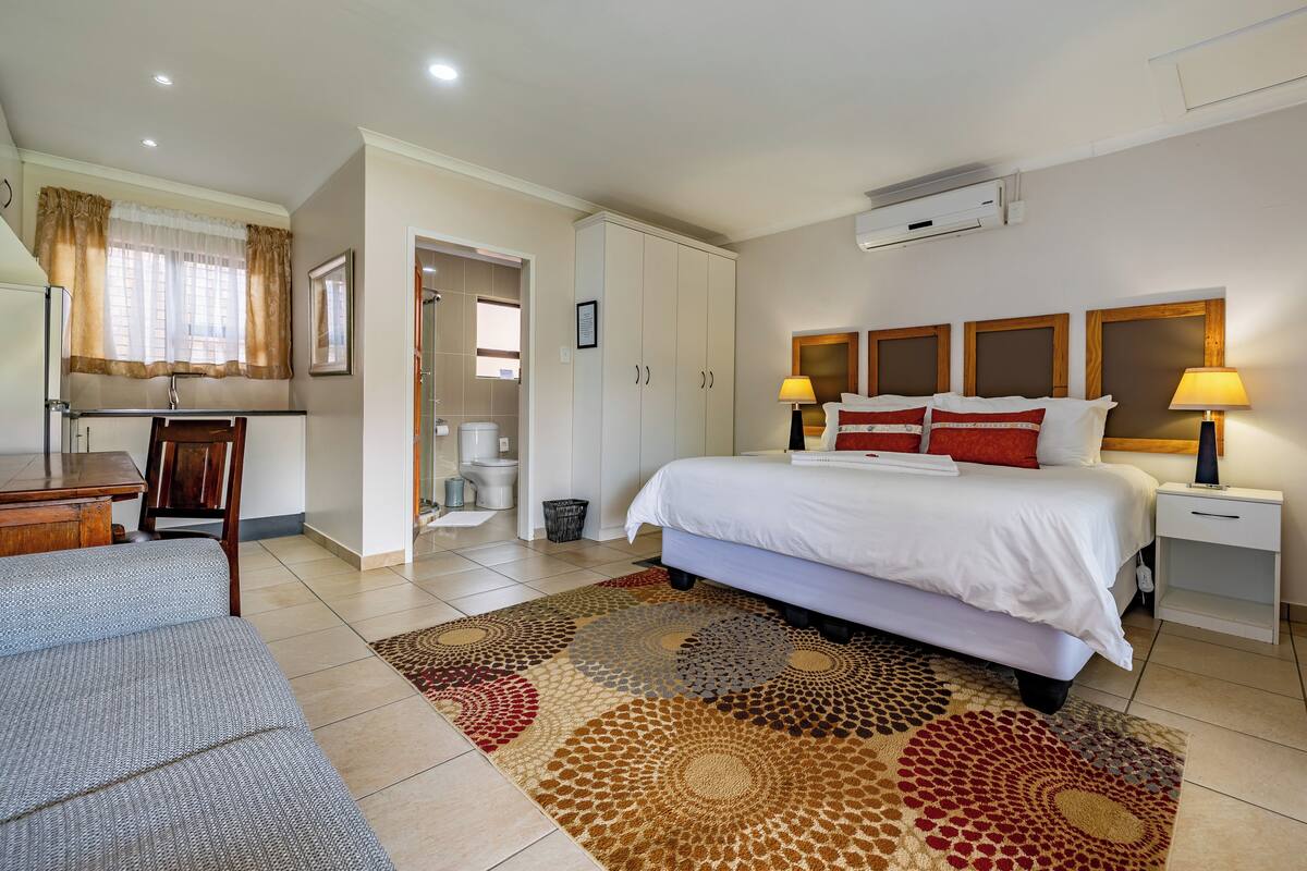 A hotel room with a bed, bedside tables, a desk, a chair, a bathroom, and a window with curtains.