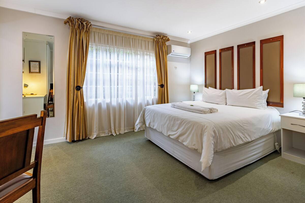 A hotel room with a bed, a desk, a chair, and a window with curtains.