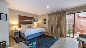 A hotel room with a bed, nightstands, a patterned rug, a sliding glass door to a balcony, and a framed picture on the wall. - Botleng Guest House (Maseru)