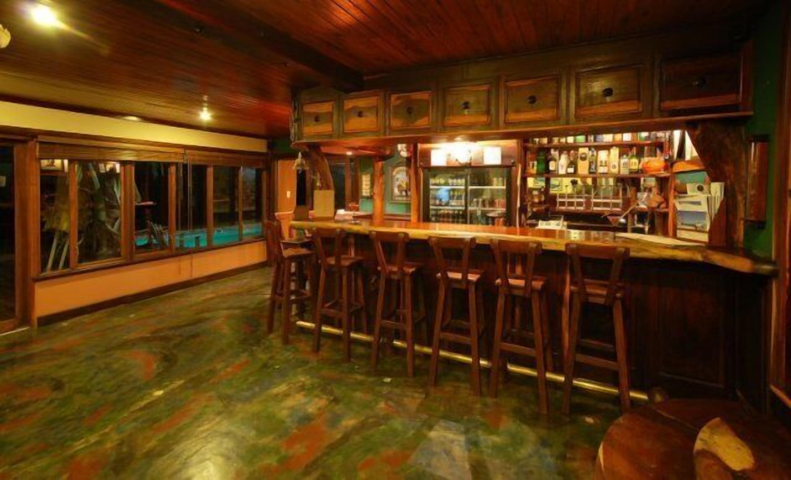 A bar area with wooden bar stools, a counter, and a view of the outside through large windows.