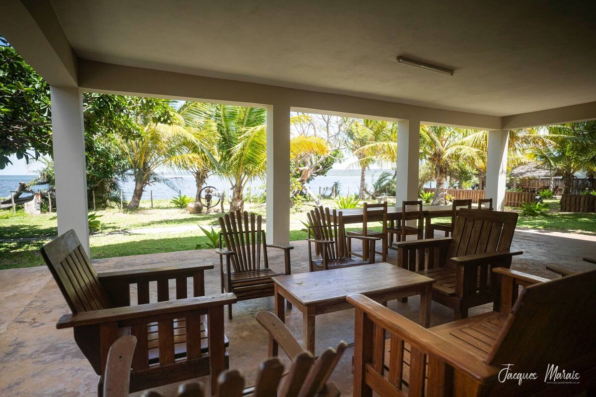 An outdoor patio area with wooden furniture and a view of the sea and palm trees.