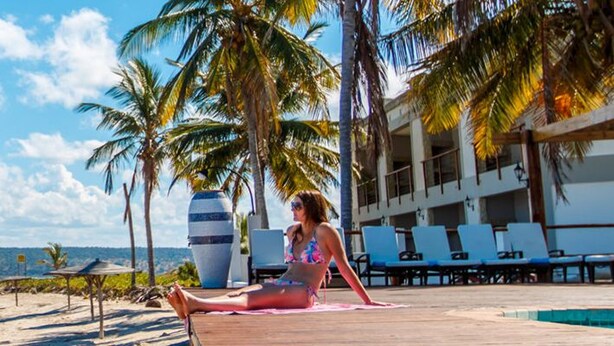 A beachside resort with a pool area, palm trees, and a view of the ocean.