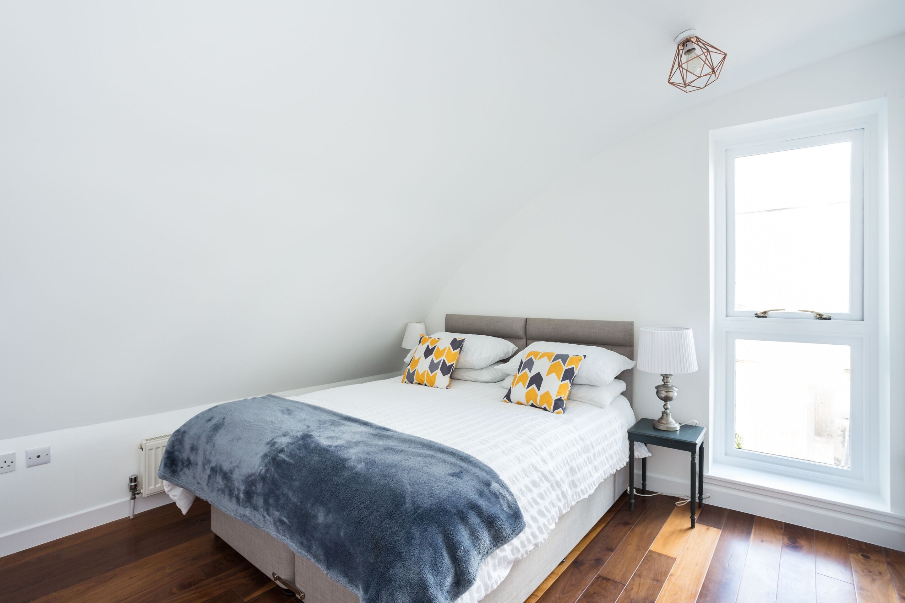 A bedroom with a bed, bedside table, lamp, and a window.