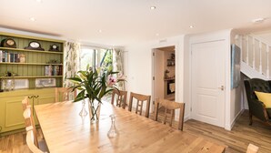 Ein Esszimmer mit Holztisch, Stühlen, einem Bücherregal und Blick zur Küche.