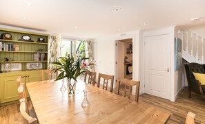 A dining room with a wooden table, chairs, a bookshelf, and a view of the kitchen. - The Crown & Kitchen (East Linton)