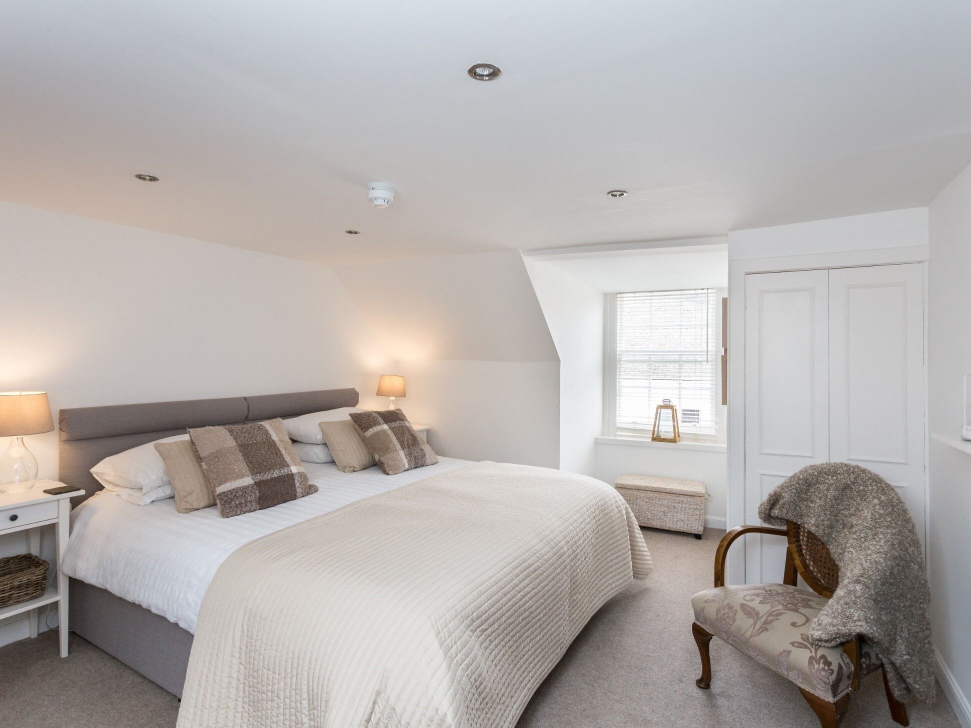 A bedroom with a bed, bedside lamps, a chair, a window, and a door.