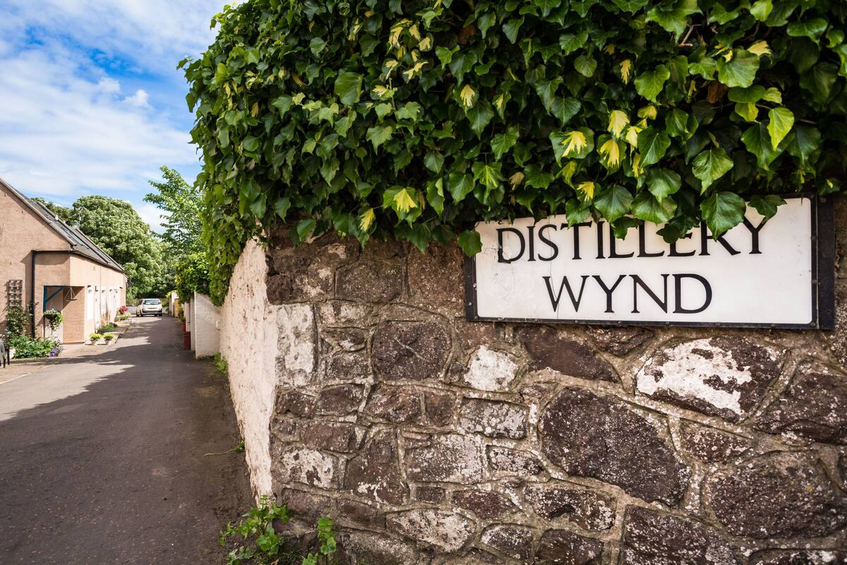 A stone wall with a sign reading 'DISTILLERY WYND' and a narrow street.