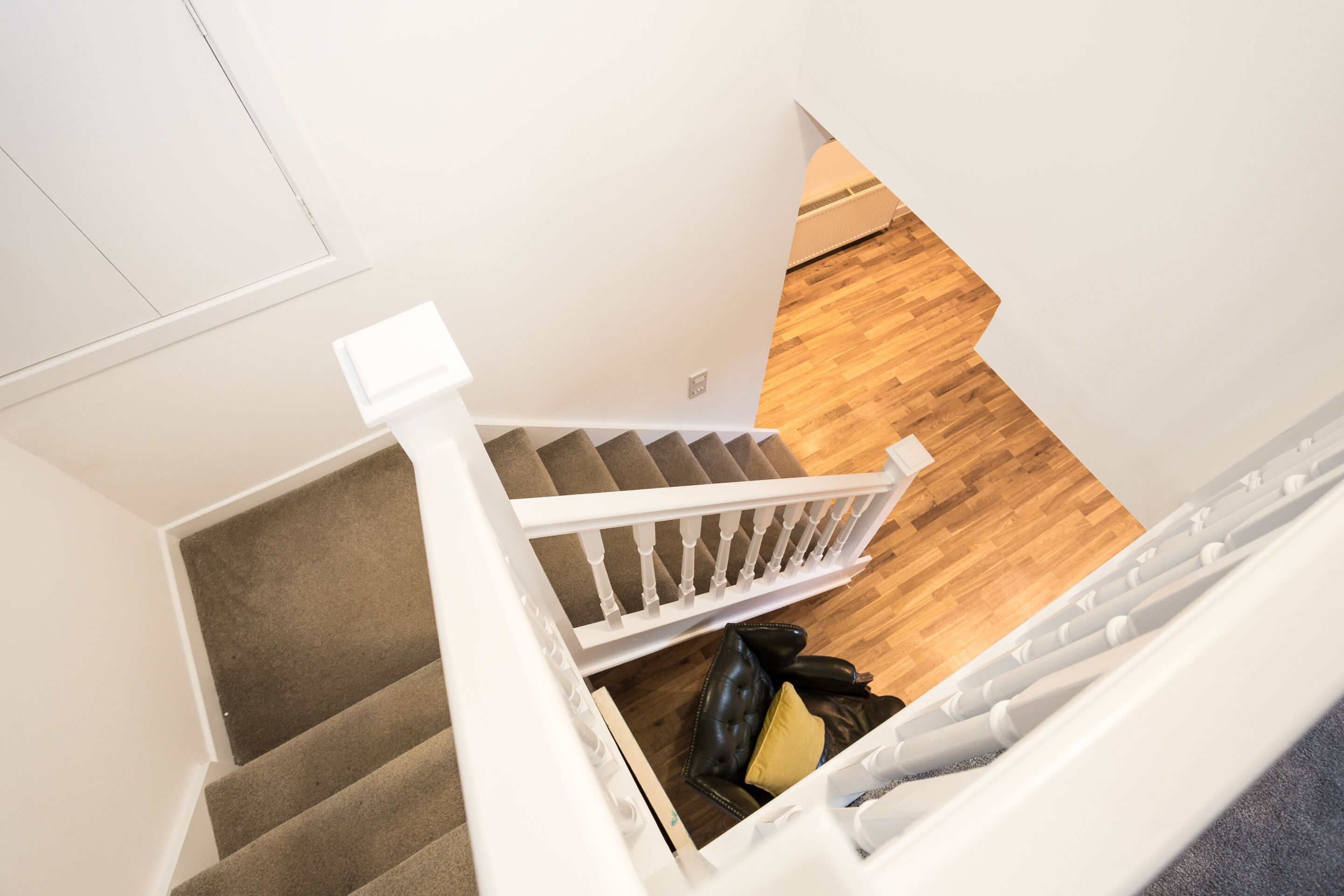 Een trap met een witte leuning, bekleed met tapijt, en een houten vloer.