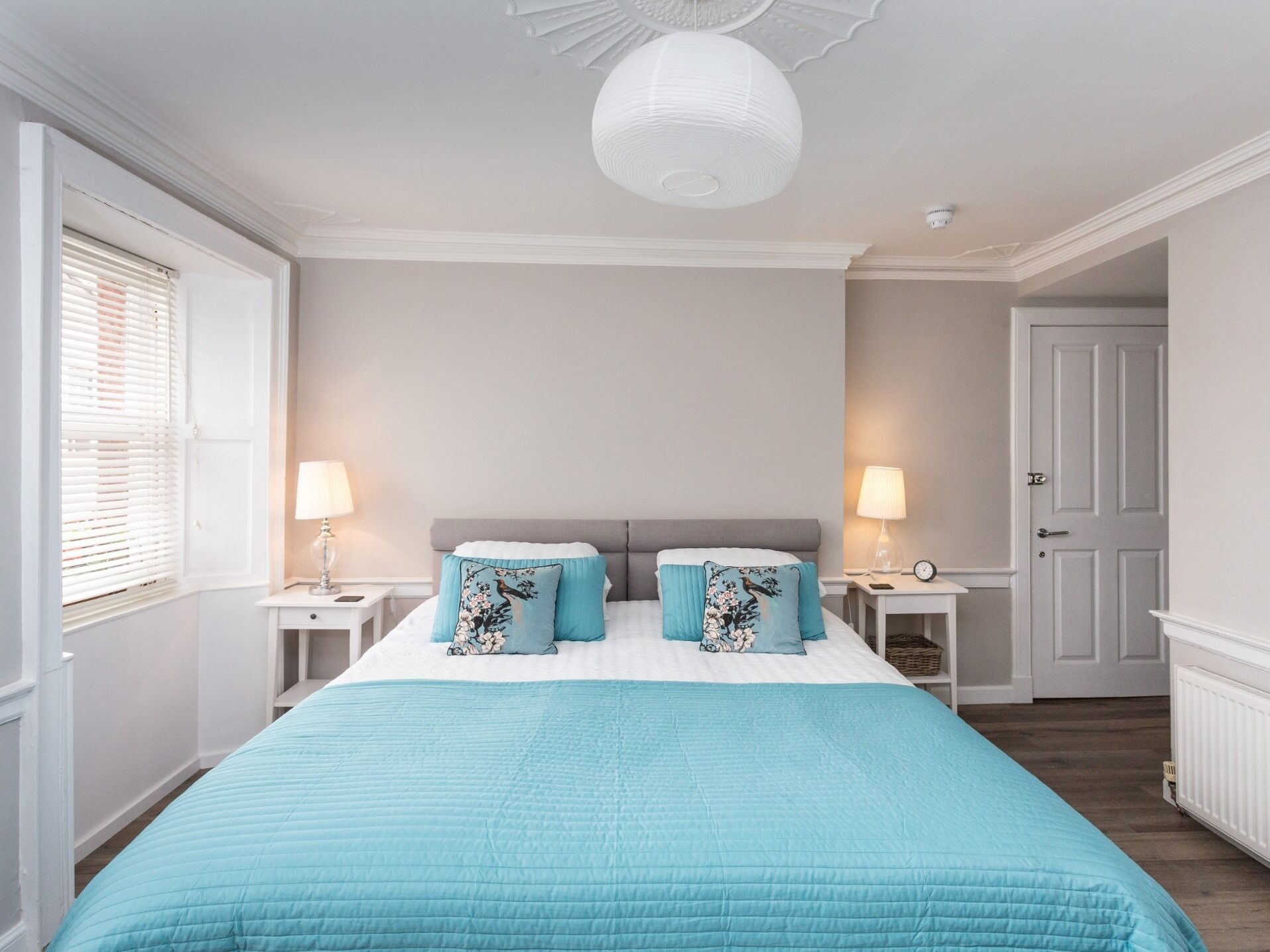 A bedroom with a large bed, two nightstands, a white ceiling, and a door.
