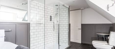 A modern bathroom with a glass-enclosed shower, white tiles, a toilet, and a bathtub.