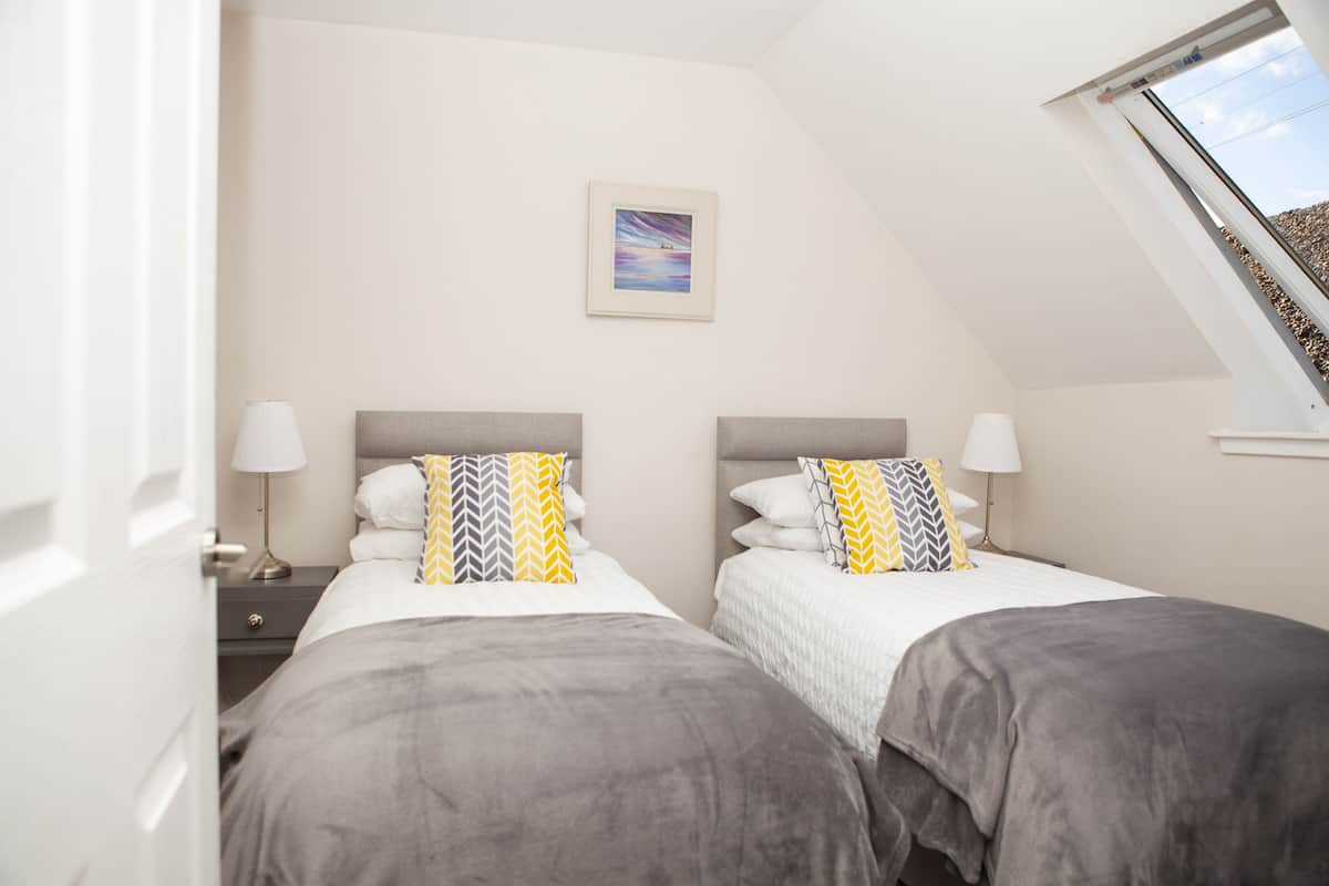 A bedroom with two beds, a nightstand, a lamp, and a framed picture on the wall.