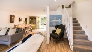 Ein Wohnzimmer mit einer Couch, einem Esstisch mit Stühlen, einem Bücherregal, einem schwarzen Ledersessel und einer Treppe.