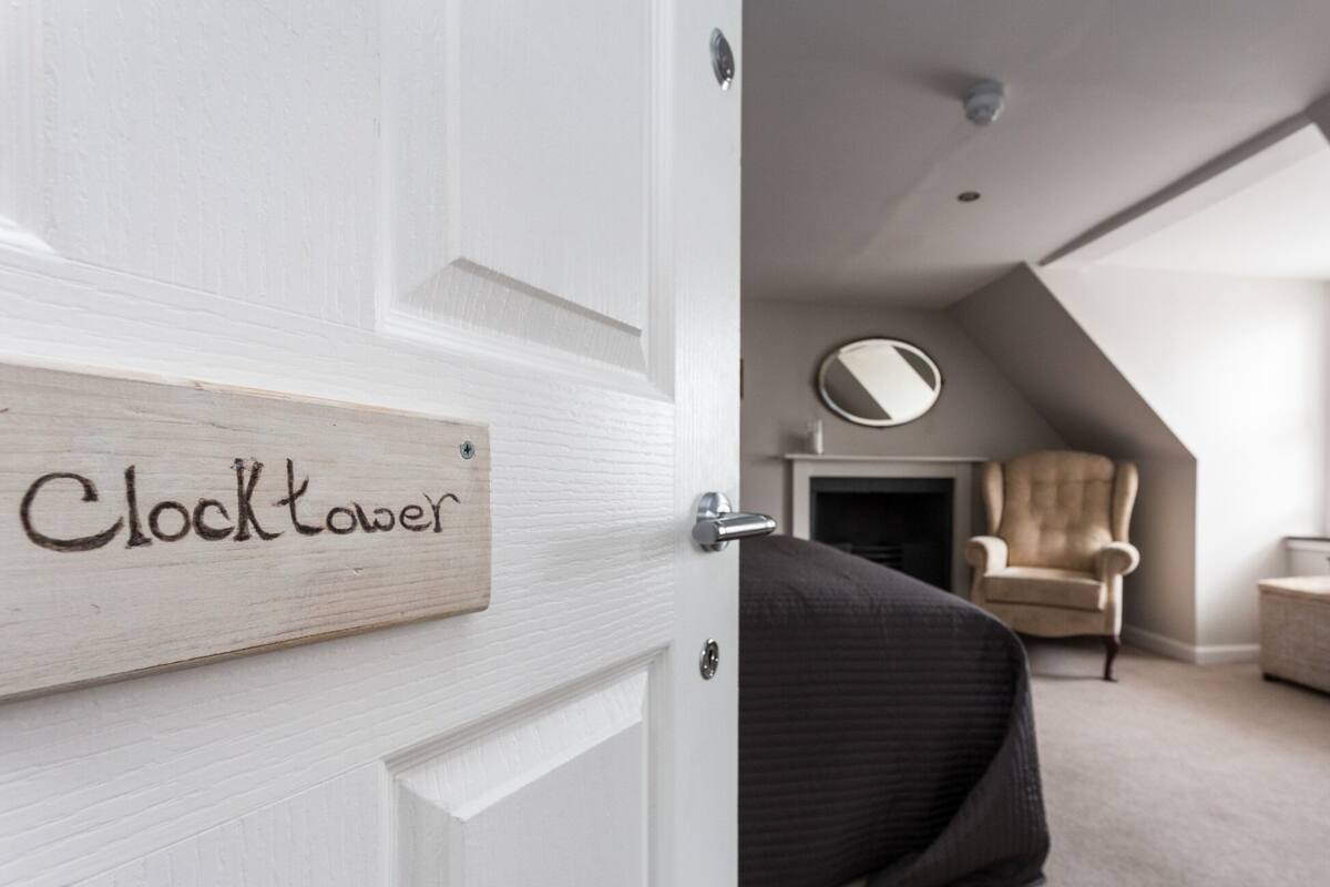 A bedroom with a bed, a chair, a fireplace, and a door labeled "Clocktower".