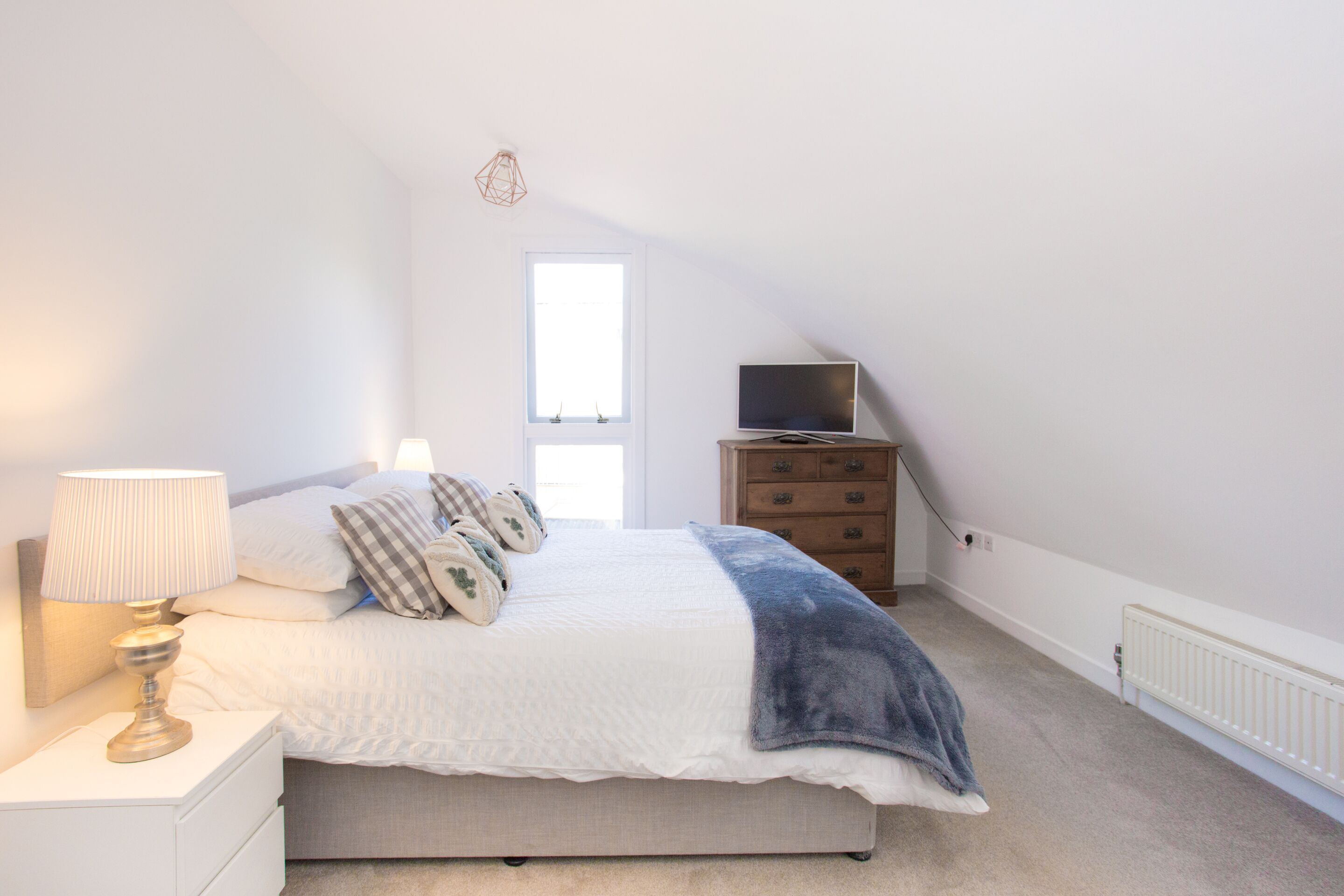 Une chambre à coucher comprenant un lit, une table de chevet, une commode, un téléviseur et une fenêtre.