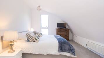 Une chambre à coucher comprenant un lit, une table de chevet, une commode, un téléviseur et une fenêtre.
