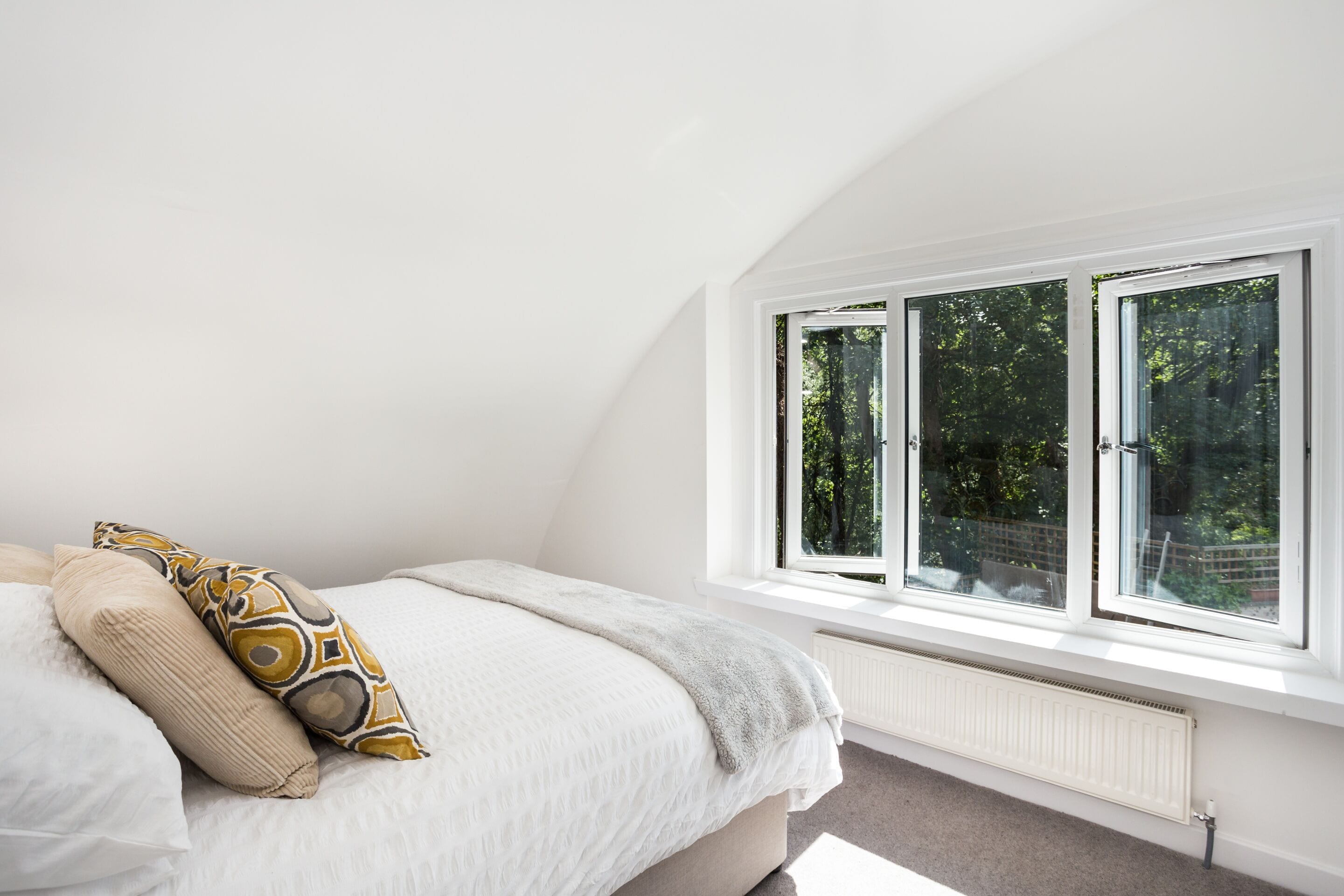 A bedroom with a large window, a bed with patterned pillows, and a radiator.