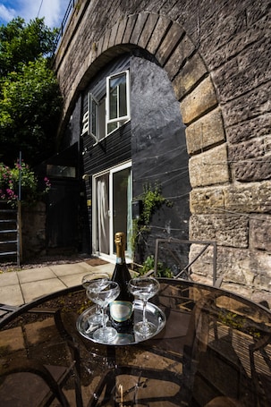 A glass table with a bottle and glasses, set against a stone wall with a door and window.. The Crown & Kitchen