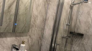 A modern bathroom with a marble backsplash, a glass-enclosed shower, a white sink with a soap dispenser, and a mirror above the sink. - Ashfield Hotel (Huddersfield)