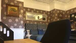 A room with a wooden table, a tufted headboard bed, a mirror, and a framed picture on the wall. - Ashfield Hotel (Huddersfield)