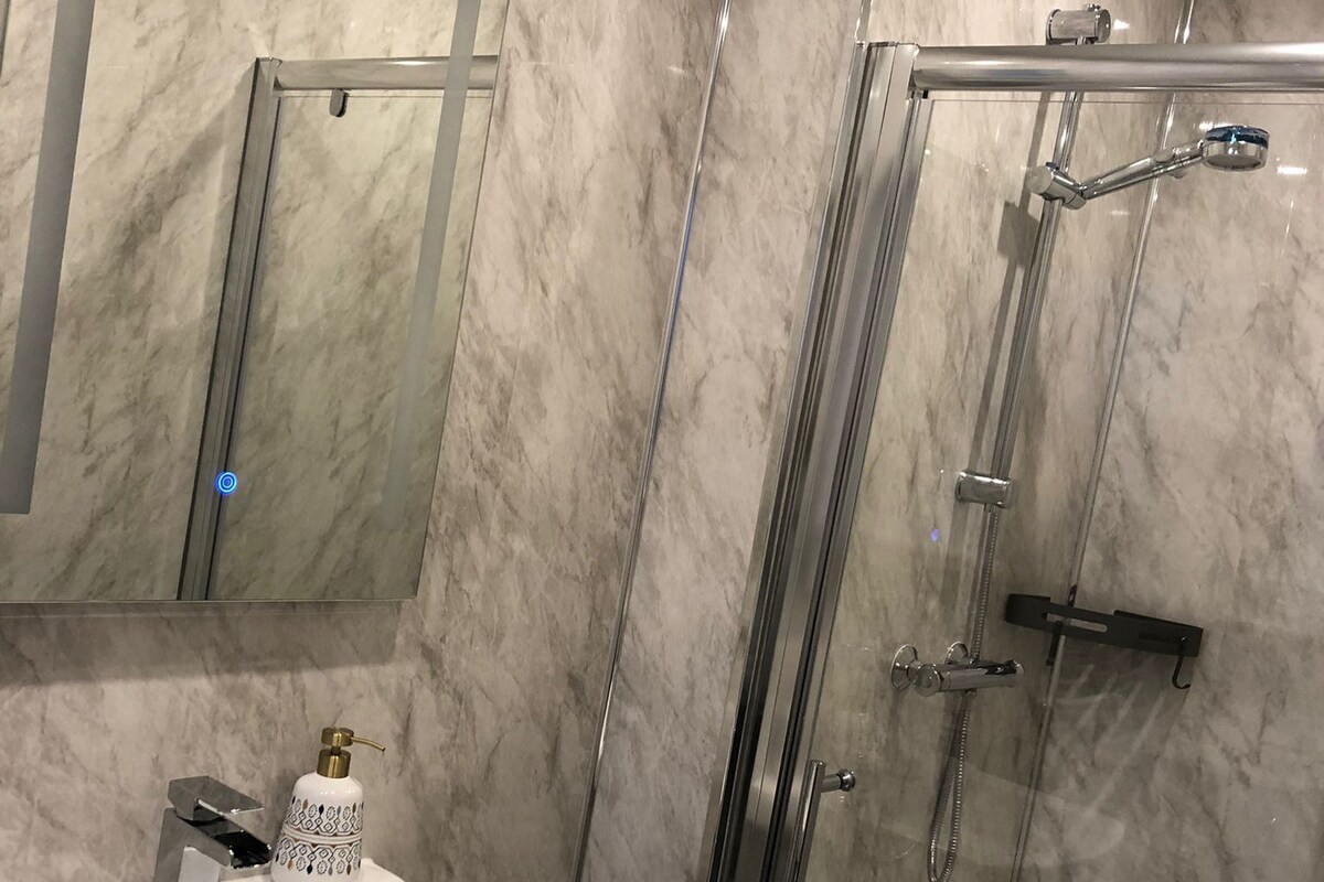 Un baño con pared de mármol, un lavamanos con grifo moderno y cabina de ducha con paredes de vidrio.