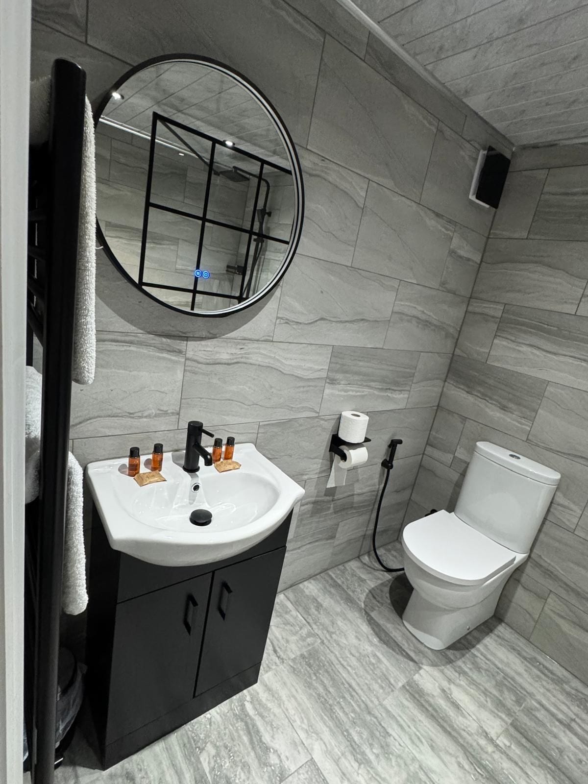 Une salle de bain avec un lavabo blanc, des meubles noirs, un miroir rond et des toilettes.