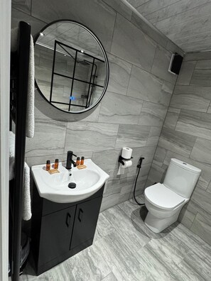 A bathroom with a white sink, black cabinets, a round mirror, and a toilet. - Ashfield Hotel (Huddersfield)