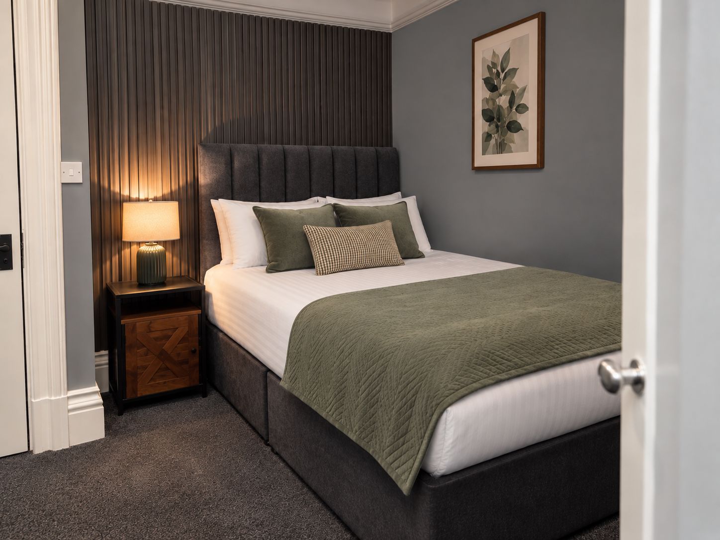 A bedroom with a bed, a bedside table, a lamp, and a framed picture on the wall.