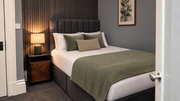A bedroom with a bed, a bedside table, a lamp, and a framed picture on the wall.