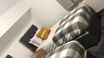 Quarto com cama, travesseiros, mesa de cabeceira e radiador.