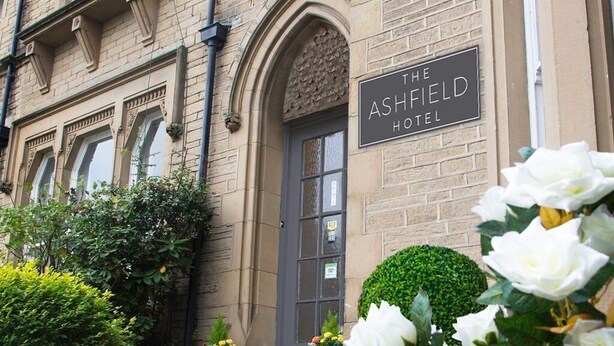The Ashfield Hotel with a classic brick facade, a prominent entrance, and a well-maintained garden with potted plants and flowers. - Ashfield Hotel (Huddersfield)