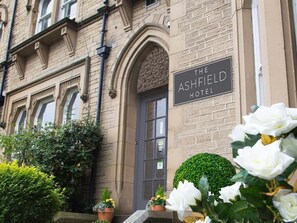 The Ashfield Hotel with a classic brick facade, a prominent entrance, and a well-maintained garden with potted plants and flowers. - Ashfield Hotel (Huddersfield)