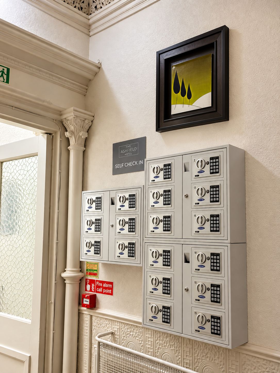 A self check-in area at The Ashfield Hotel with numbered lockers and a fire alarm call point.