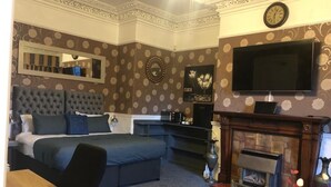 A bedroom with a large bed, a TV, a fireplace, and a mirror. - Ashfield Hotel (Huddersfield)