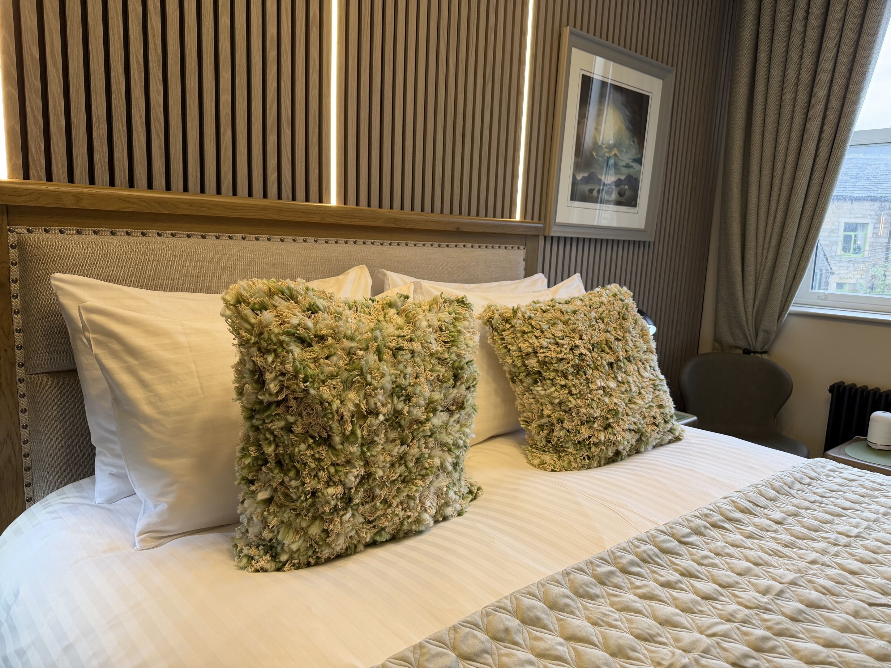 A bed with a quilted cover, two pillows, a headboard, and a framed picture on the wall.