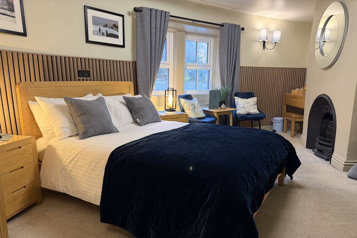 A neatly arranged bedroom with a large bed, bedside tables, a chair, a small table, and a fireplace.
