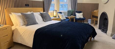 A neatly arranged bedroom with a large bed, bedside tables, a chair, a small table, and a fireplace.