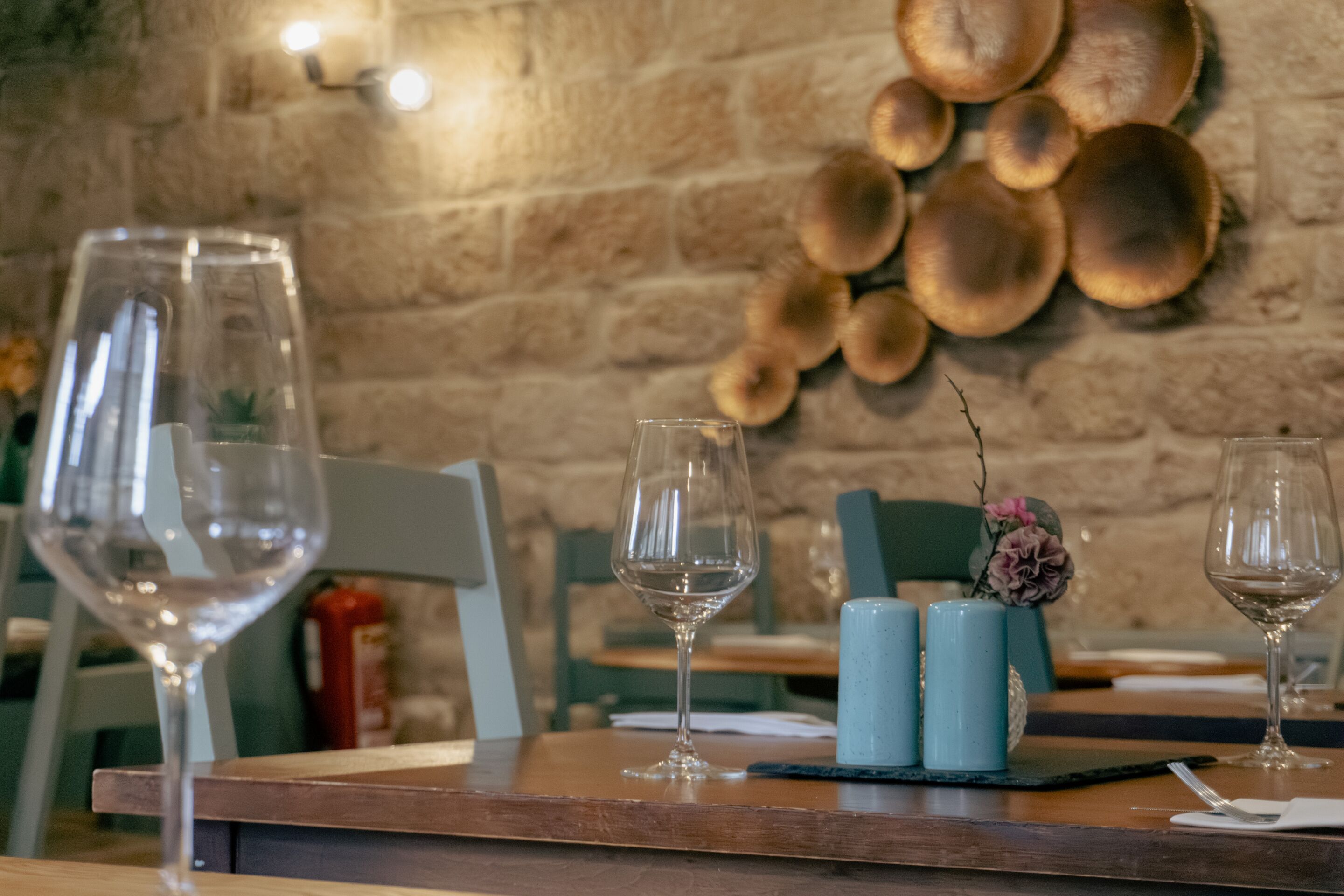 A restaurant setting with a wooden table, two empty wine glasses, and a decorative wall with wooden plates.