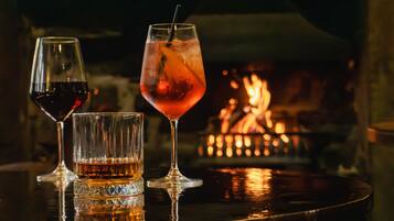 Tres vasos de bebidas sobre una superficie reflectante, con un fuego de fondo.