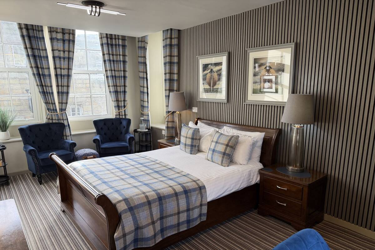 A hotel room with a large bed, two armchairs, a side table, and a lamp.