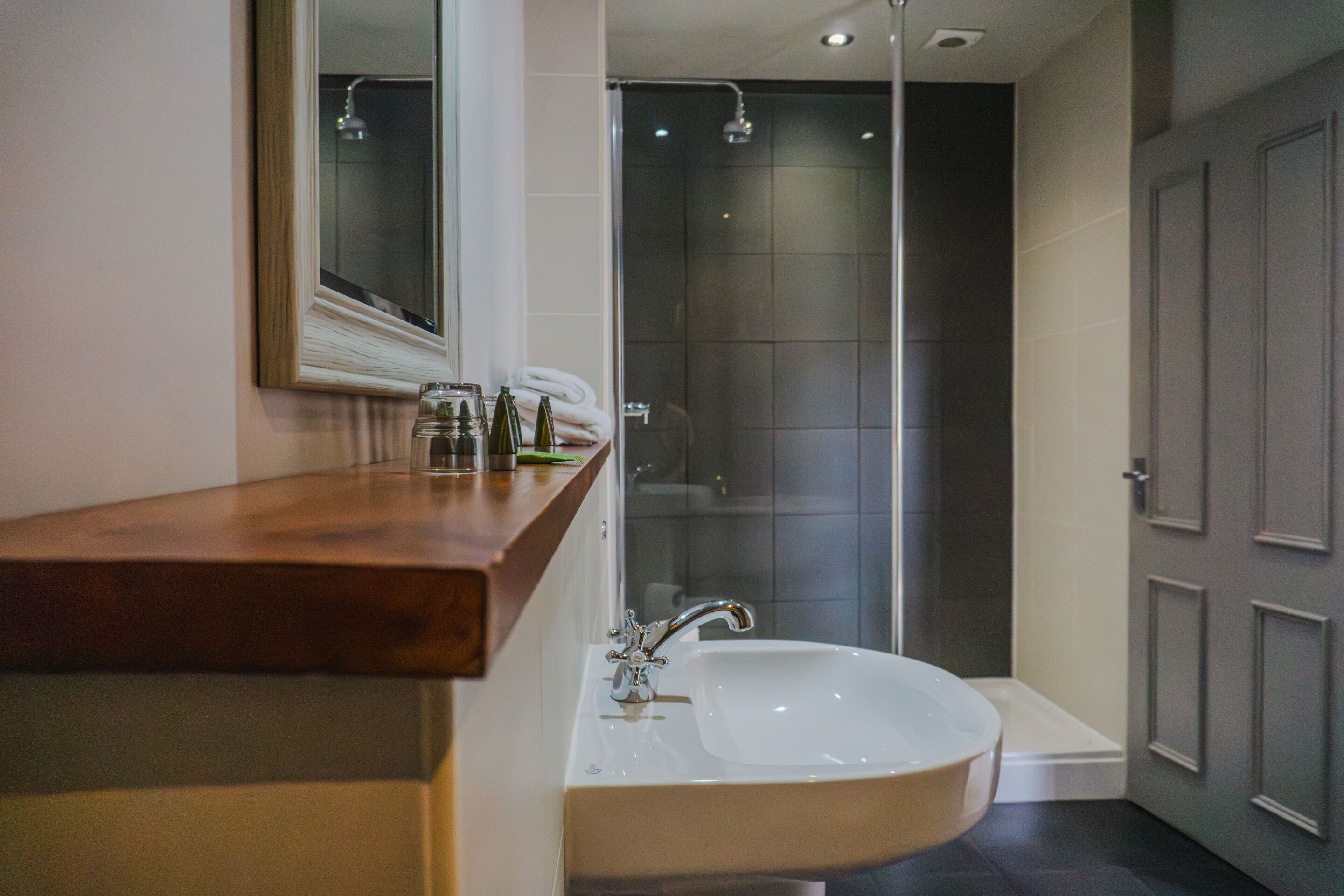 Une salle de bain moderne avec un meuble-lavabo en bois, un lavabo blanc et une cabine de douche en verre.