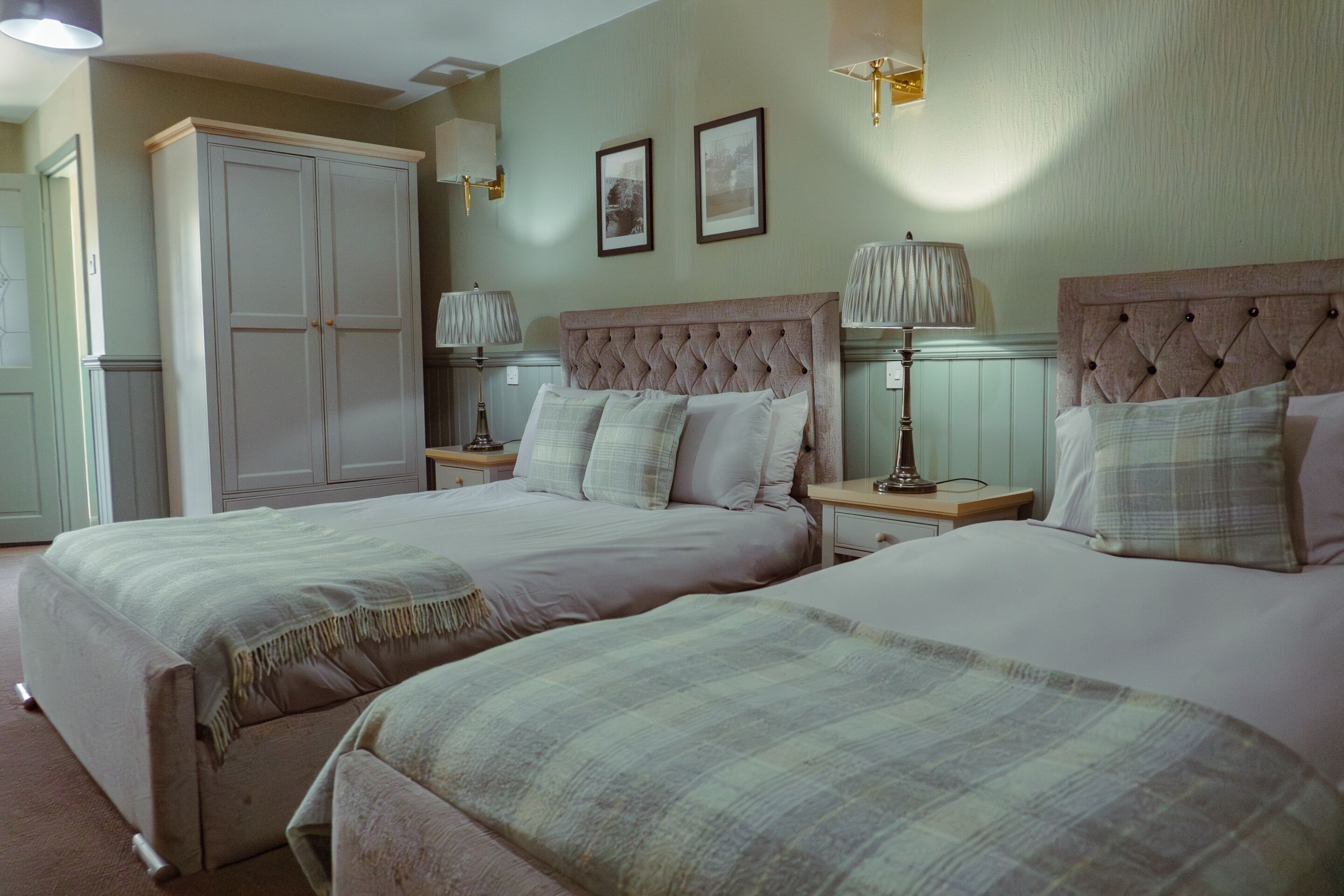 A bedroom with two beds, a wardrobe, bedside lamps, and framed pictures on the wall.