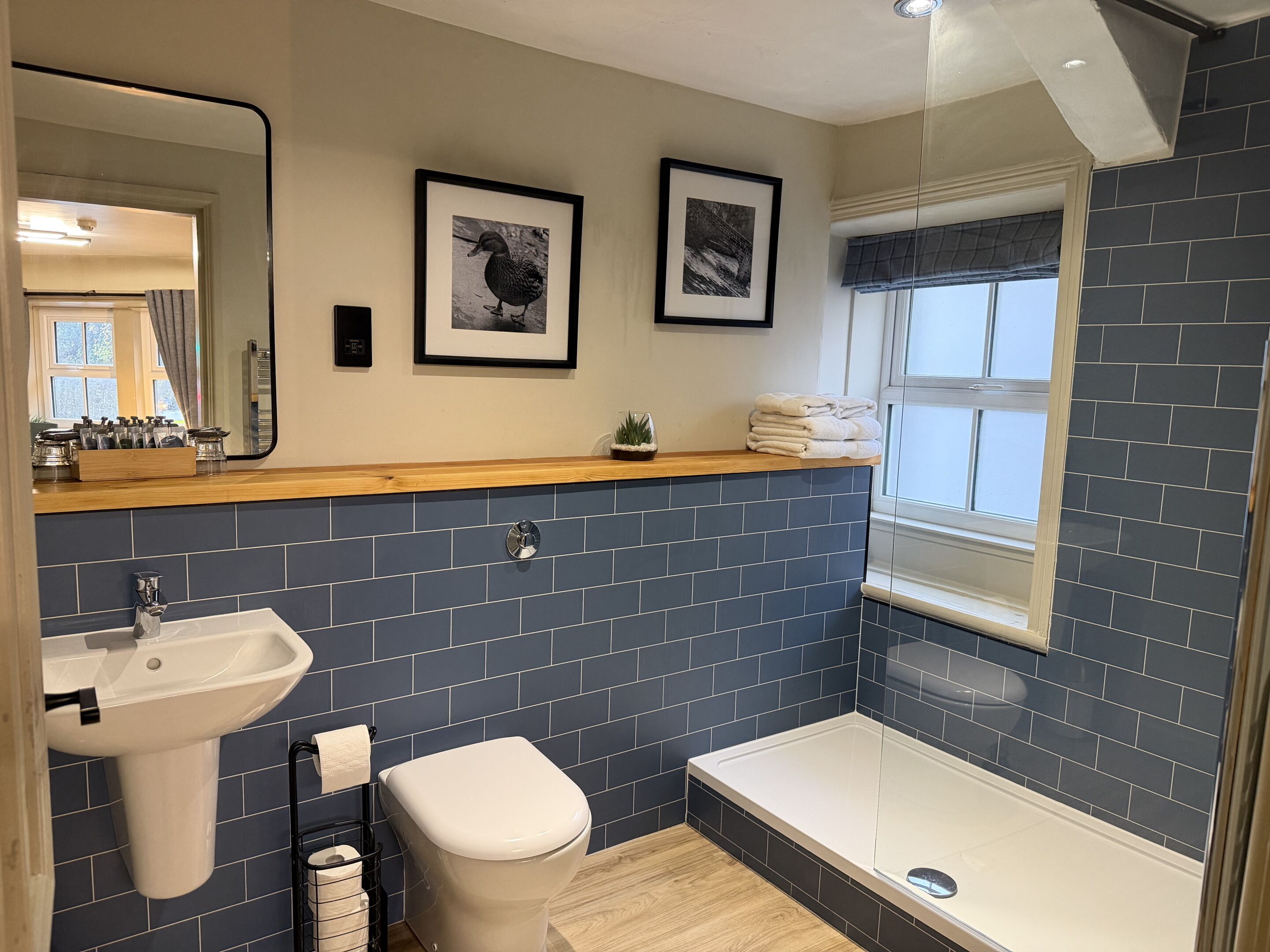 Un baño moderno con lavamanos, inodoro y bañera, con baldosas azul oscuro y detalles de madera.